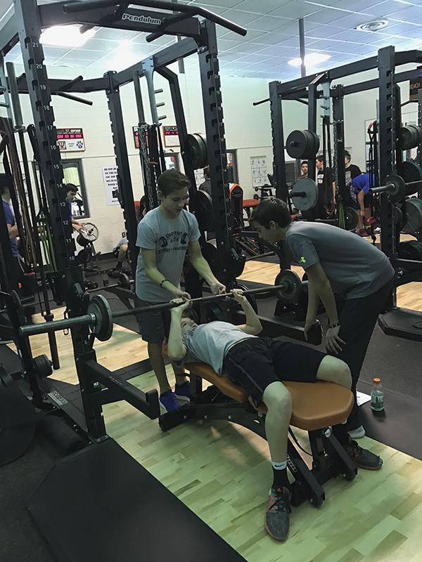 With a spotter for safety, athletes bench press in the weight room after school.