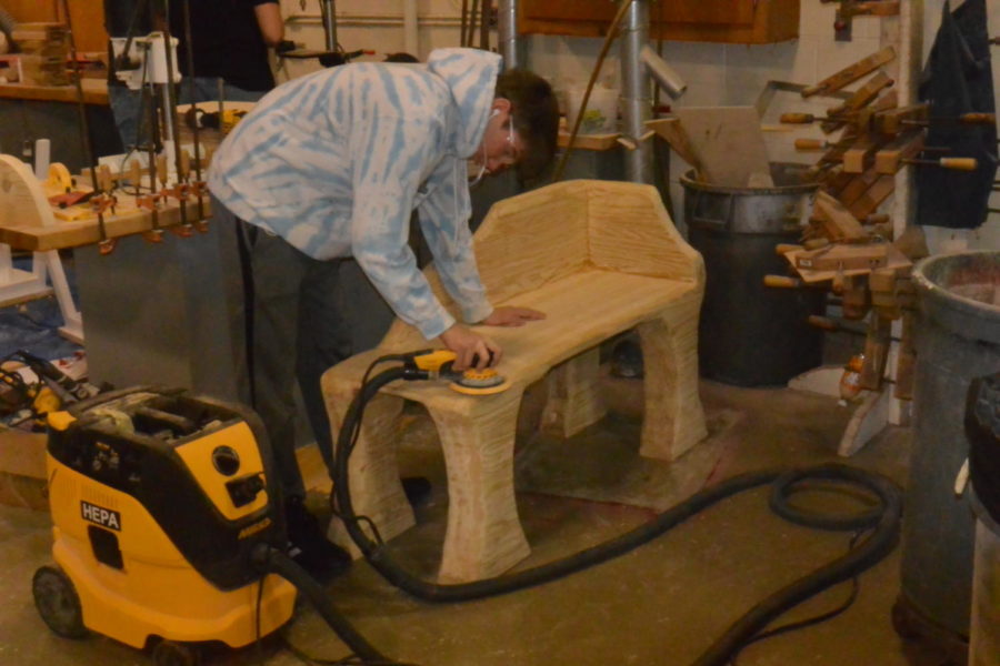 In the back of the shop, Henry Ford II junior Andrew Kovach sands a hand-carved bench.