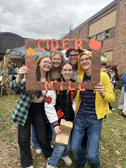 Choir teacher Jeremy Sloat, seniors Carley Davis, Logan Spillane, Caitlyn Seal, and junior Johnothan McCabe pose with the Cider mill photo frame in Utica’s courtyard.